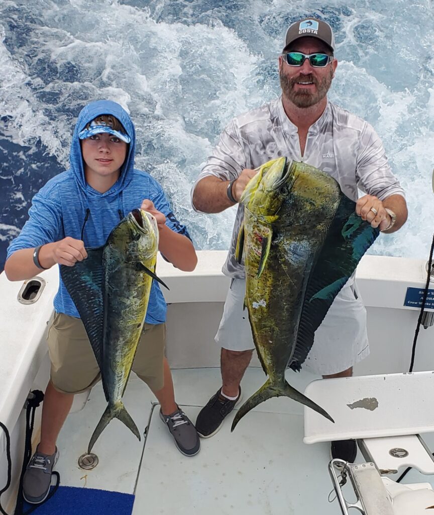 Two people proudly holding large caught fish on a boat.